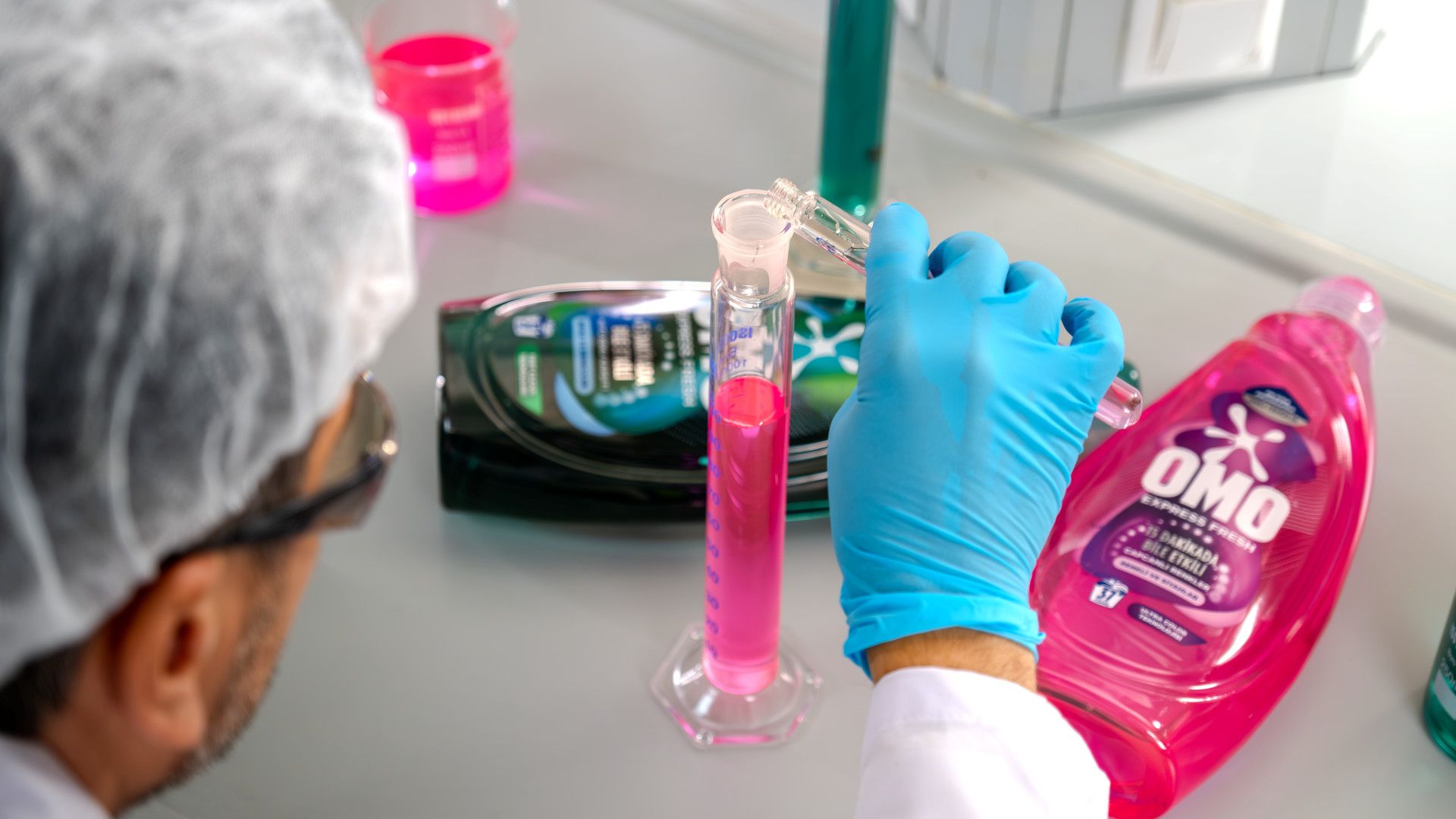 Laboratuvar önlüğüyle bir araştırmacı pembe Omo Express Fresh varyantını lab tüpüne dolduruyor.