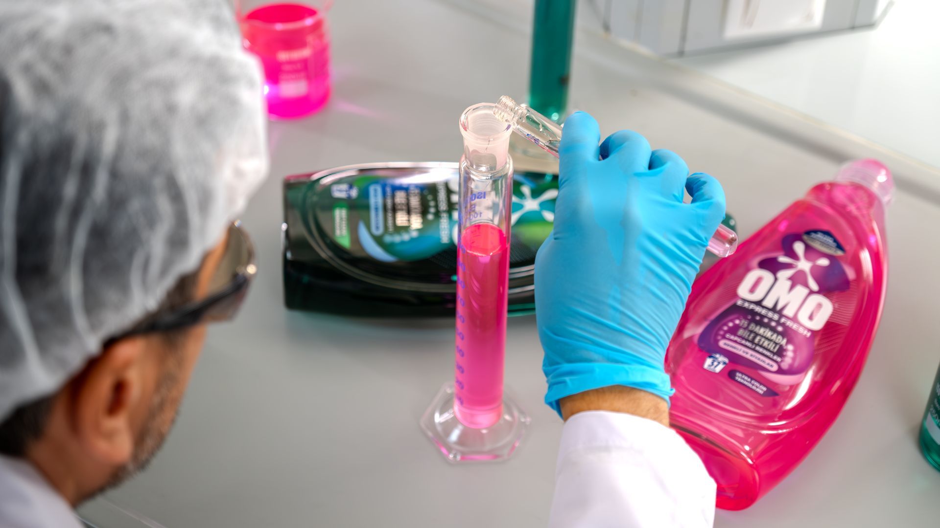 Laboratuvar önlüğüyle bir araştırmacı pembe Omo Express Fresh varyantını lab tüpüne dolduruyor